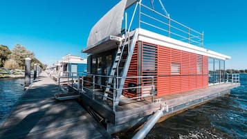 Ein schwimmendes Hausboot mit einer überdachten Terrasse, einer Treppe und einem Geländer.