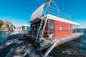 A floating houseboat with a covered deck, a staircase, and a railing.