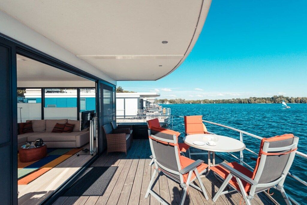 Une terrasse moderne avec un canapé et des fauteuils, donnant sur une étendue d’eau.