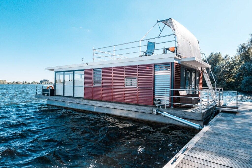 A houseboat with a covered deck, a small outdoor seating area, and a dock extending into the water.