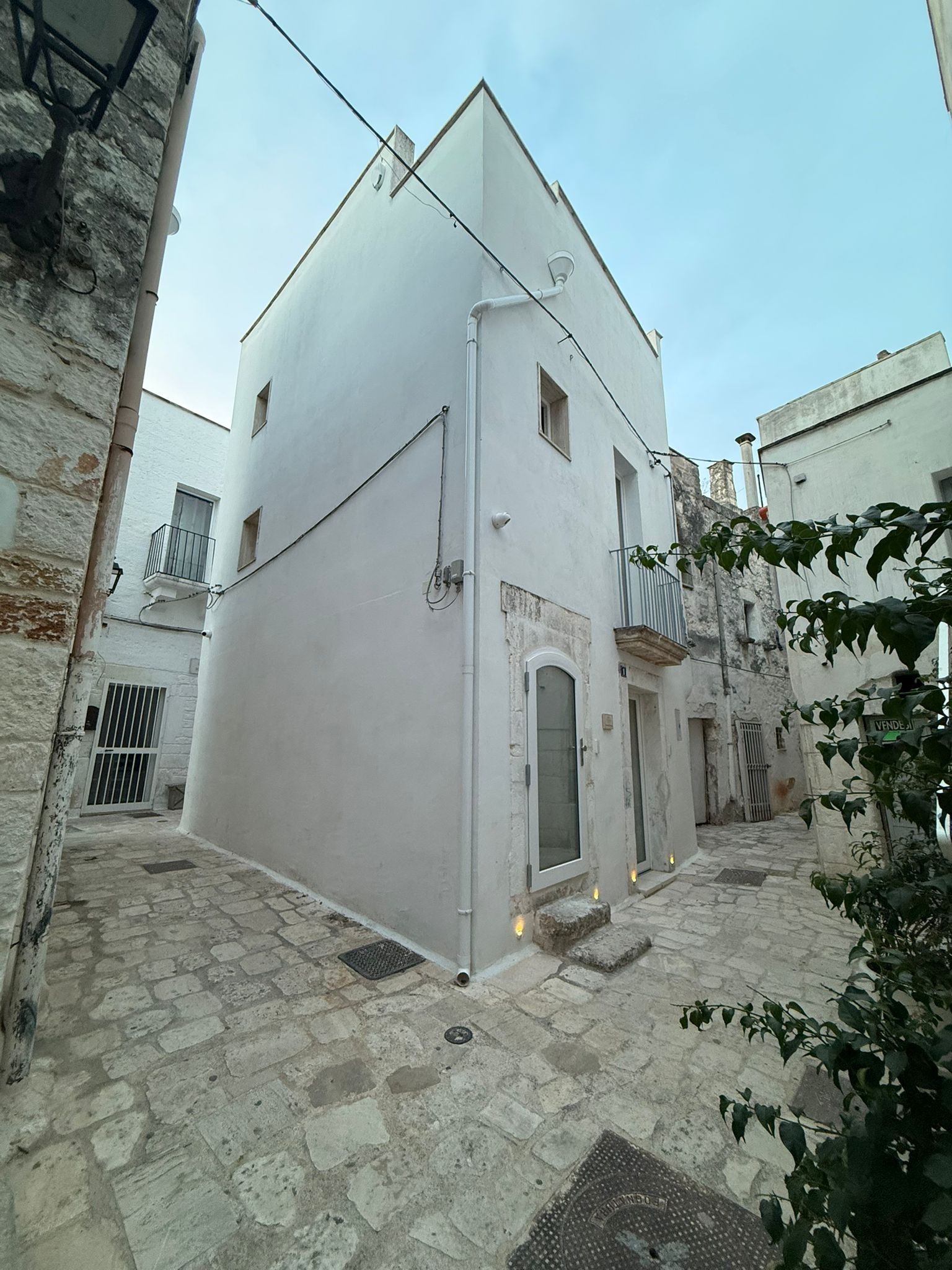 Una calle estrecha con un edificio blanco que tiene un pequeño balcón y una puerta.