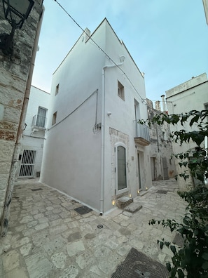 Una calle estrecha con un edificio blanco que tiene un pequeño balcón y una puerta.