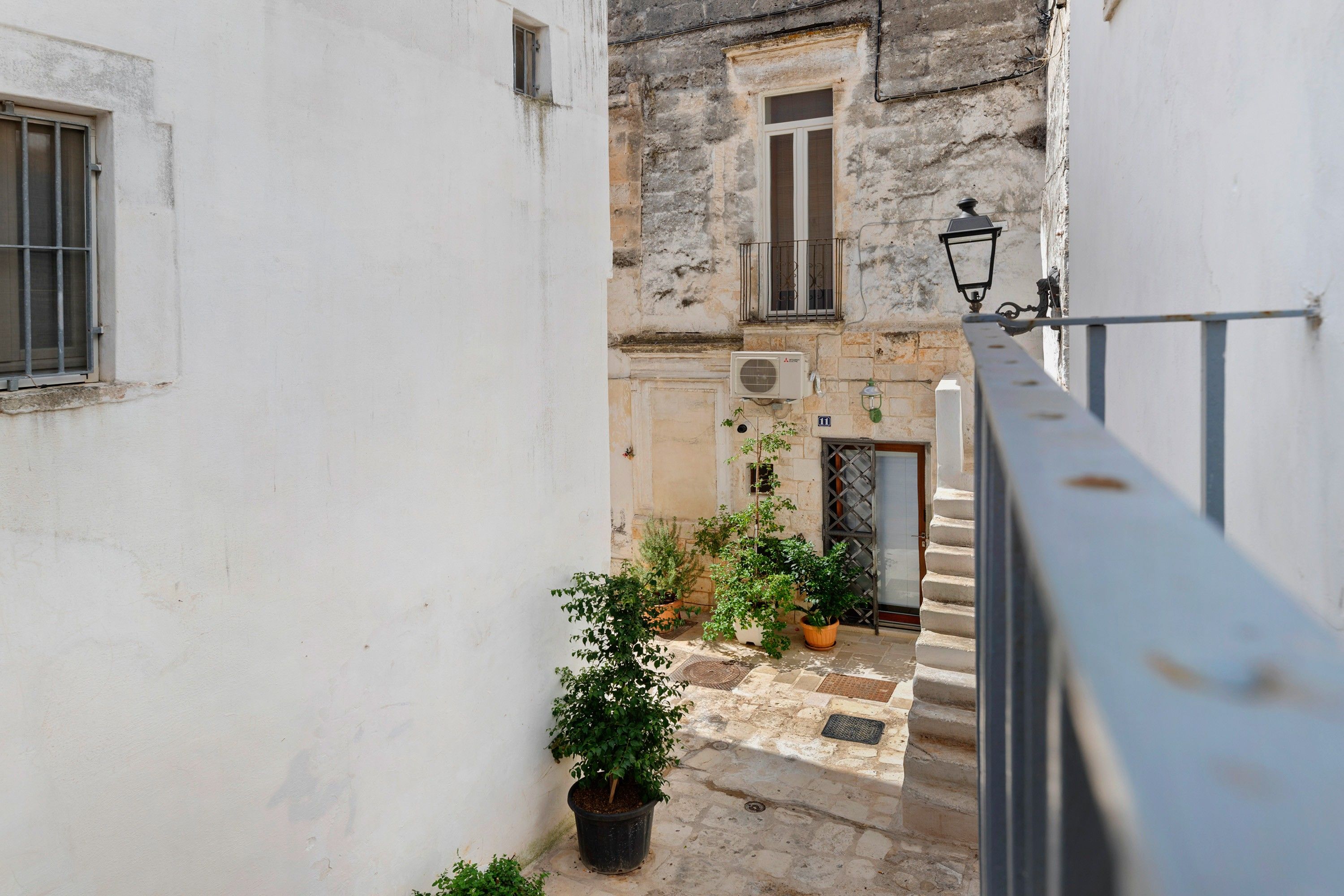 Un callejón estrecho con una escalera que conduce a un edificio con una ventana y un equipo de aire acondicionado. Hay plantas en macetas en el suelo.