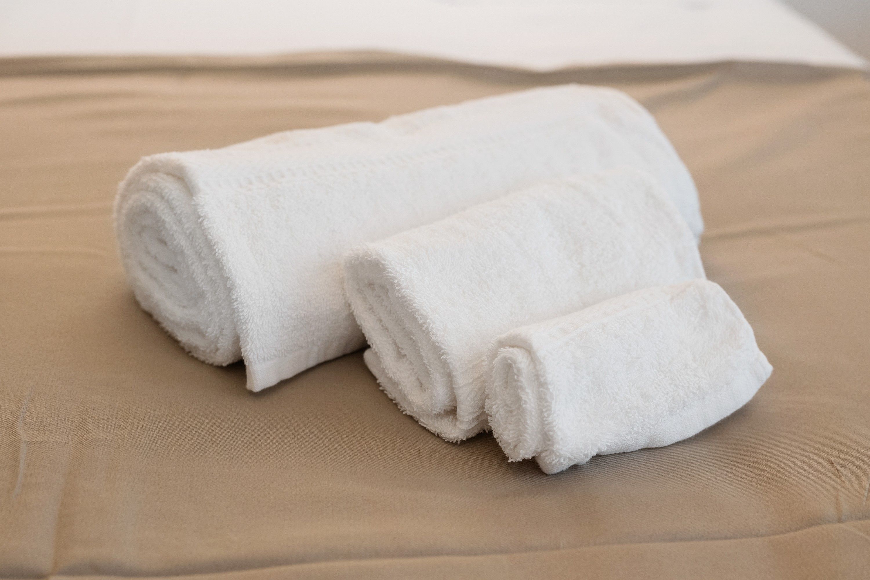 Two rolled white towels on a beige bedspread.