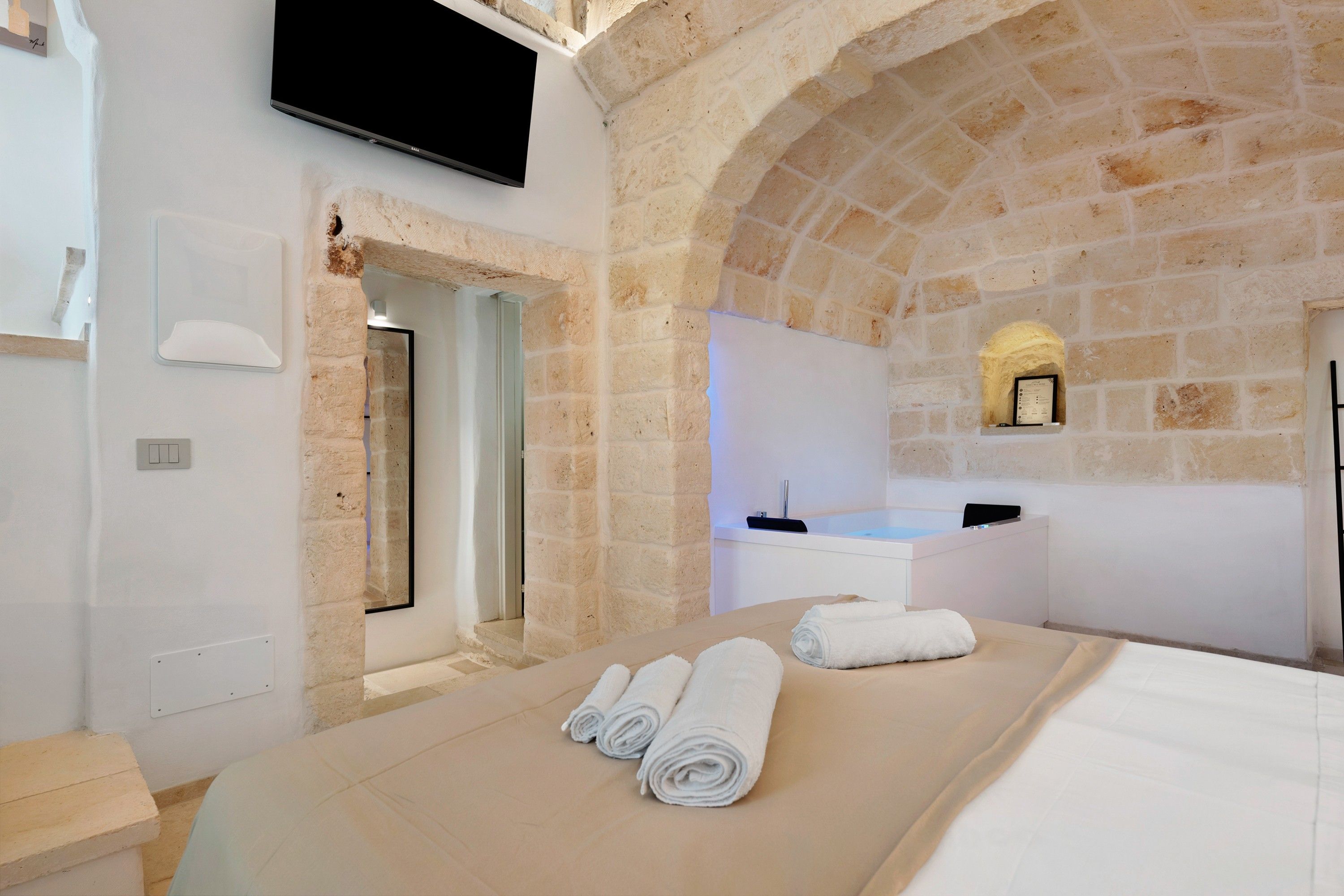 A modern bathroom with a stone arch, a bathtub, and a flat-screen TV mounted on the wall.