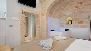 A modern bathroom with a stone arch, a bathtub, and a flat-screen TV mounted on the wall.