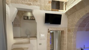 Un dormitorio con pared de piedra, televisión de pantalla plana, cama y baño con ducha.