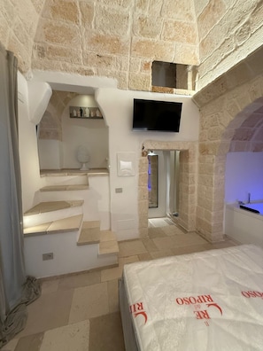 Un dormitorio con pared de piedra, televisión de pantalla plana, cama y baño con ducha.