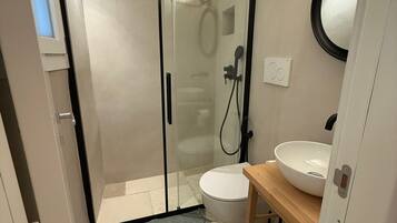 Un baño moderno con cabina de ducha de vidrio, inodoro blanco y tocador de madera con lavamanos.