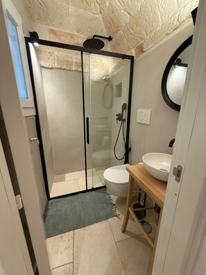 Un baño moderno con cabina de ducha de vidrio, inodoro blanco y tocador de madera con lavamanos.