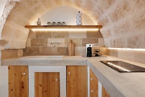 Eine Küche mit Steinrückwand, Holzschränken, einer eingebauten Spüle und einer Kaffeemaschine.