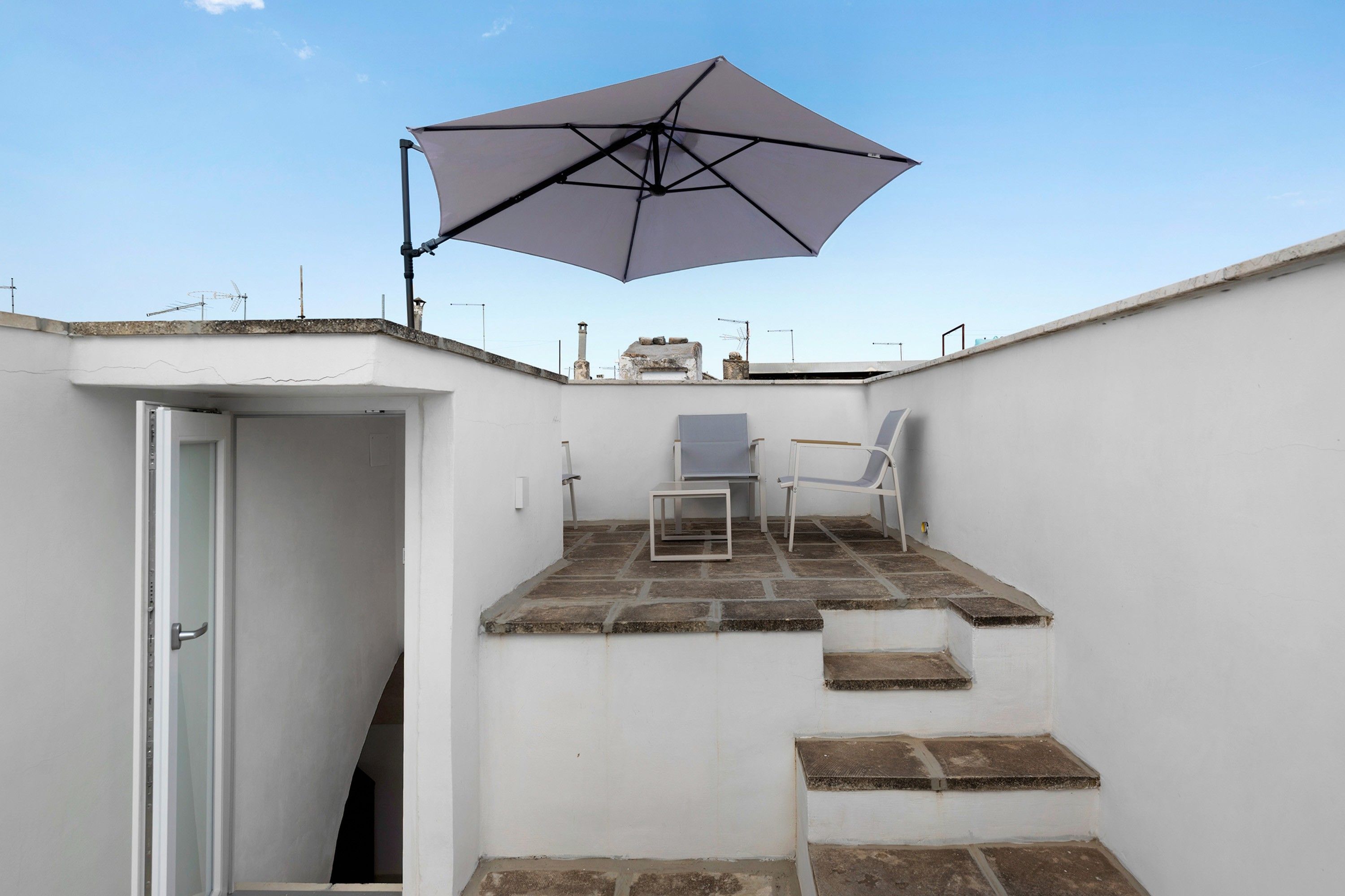 Eine kleine Terrass mit Tisch und Stühlen, einem großen Sonnenschirm und einer Tür zu einem Innenbereich.