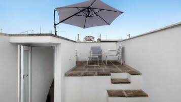 Eine kleine Terrass mit Tisch und Stühlen, einem großen Sonnenschirm und einer Tür zu einem Innenbereich.