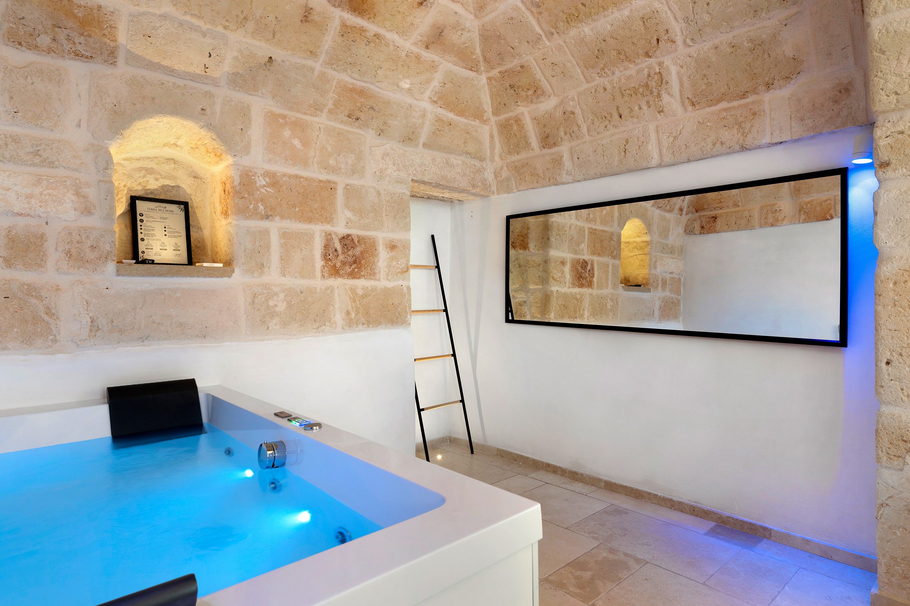 A room with a stone wall, a framed certificate, a large mirror, and a bathtub.