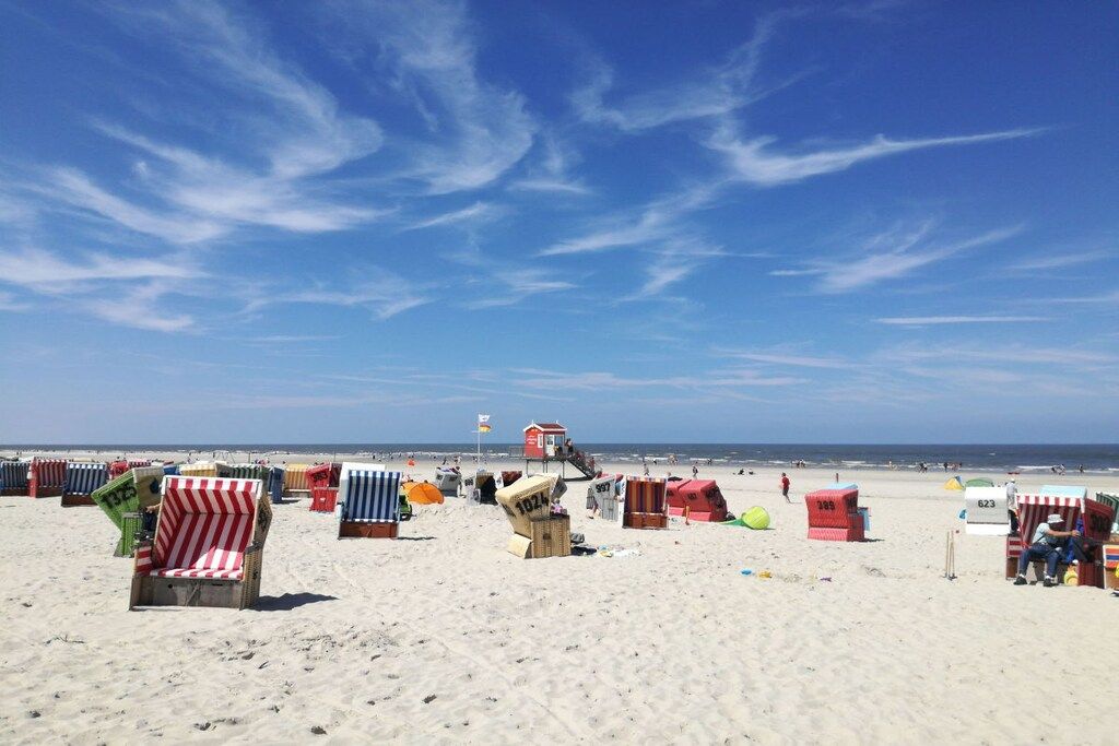 Una playa con filas de sillas y sombrillas, una torre de salvavidas y el océano al fondo.