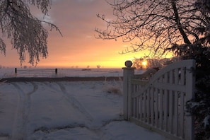 Schneebedeckte Landschaft mit einem Tor und einem Zaun im Vordergrund.