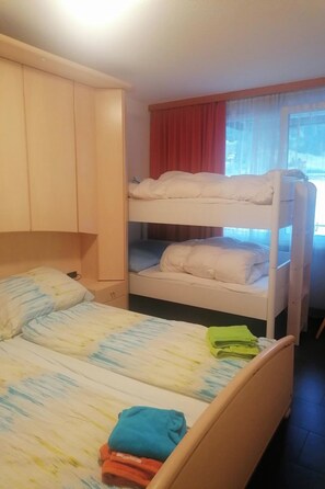Ein Schlafraum mit Etagenbett, einem Einzelbett darunter und einem hölzernen Kleiderschrank.