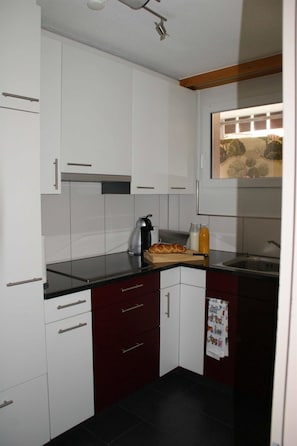 Una cucina compatta con mobili bianchi, un piano di lavoro nero e una finestra vista alberi.