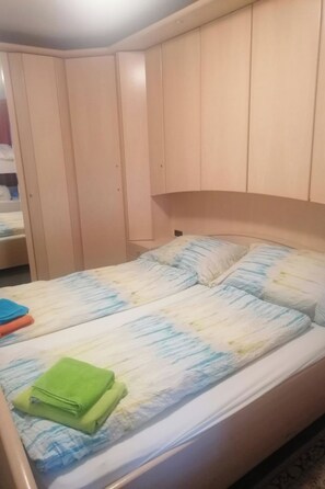 Una cama individual con una colcha estampada, una toalla verde y una almohada azul y blanca a rayas.