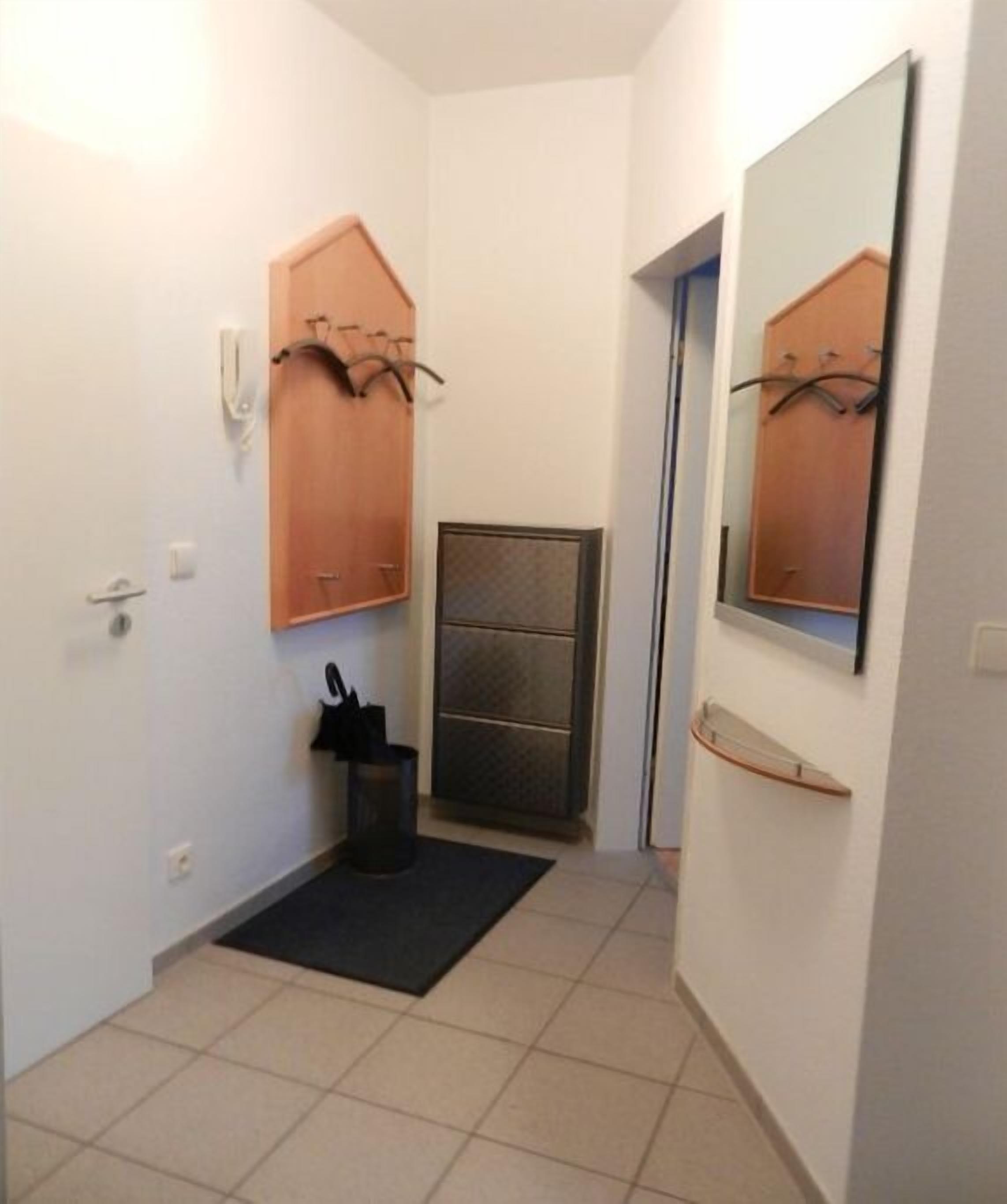 Ein schmaler Flur mit einer Tür links, einem Kleiderhaken darüber und einem Spiegel rechts.