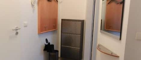 Un couloir étroit avec une porte à gauche, un porte-manteau au-dessus et un miroir à droite.