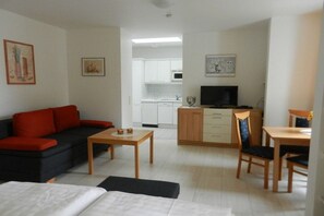 A compact living space with a sofa, a small dining table, a TV, and a kitchenette in the background. - LK 6 Remke in the Liebeskind house (Binz)