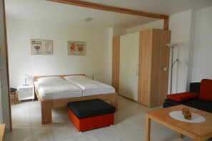 A bedroom with a bed, a nightstand, a wardrobe, a red ottoman, a wooden table, and a floor lamp. - LK 6 Remke in the Liebeskind house (Binz)