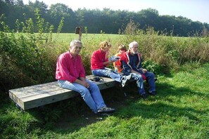 Four individuals seated on a wooden bench in a grassy outdoor setting. - Holiday apartment with 1 bedroom (Ostbevern)