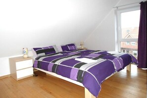 A bedroom with a bed, a nightstand, a lamp, and a window with curtains. - Holiday apartment with 1 bedroom (Ostbevern)
