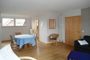 A room with a dining table, chairs, a sofa, a window, a door, and a radiator. - Holiday apartment with 1 bedroom (Ostbevern)