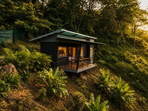 Una cabaña moderna con balcón, rodeada de abundante vegetación.