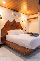 A wooden bed with a mountain headboard, white bedding, and a wall-mounted air conditioner.