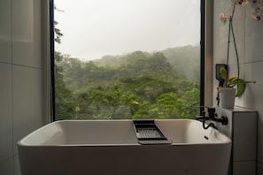 A bathroom with a bathtub, a window, and a potted orchid.