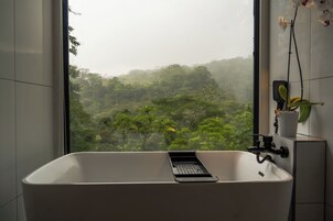 A bathroom with a bathtub, a window, and a potted orchid.