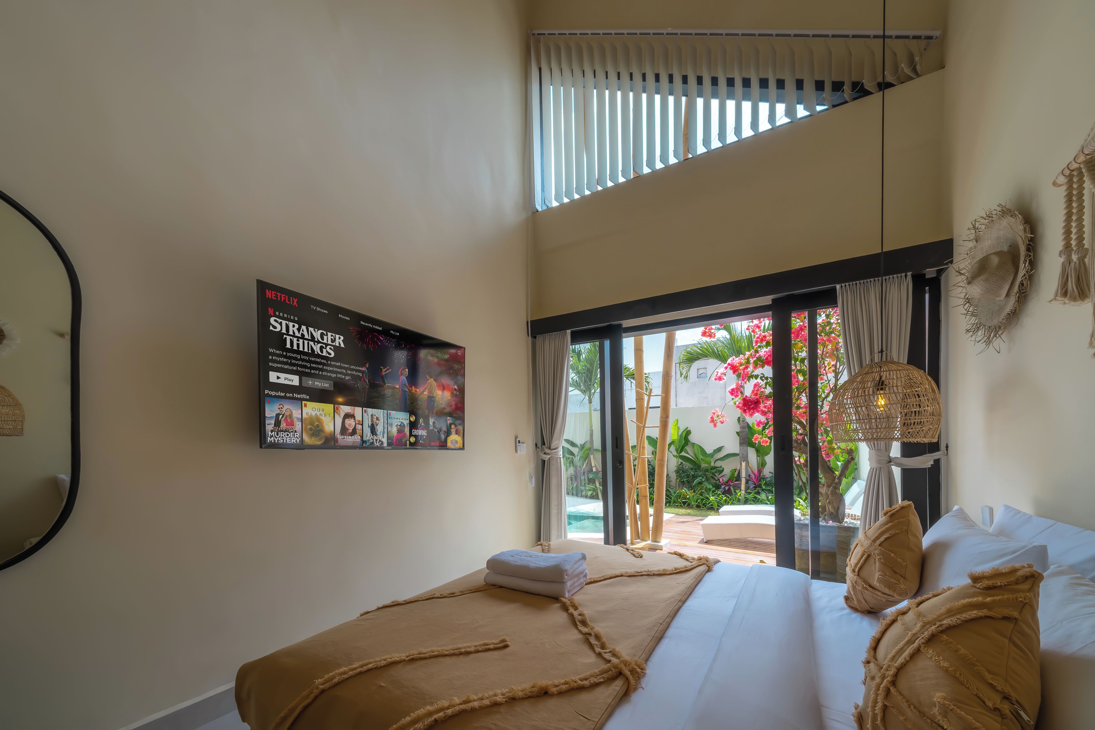 Habitación de hotel con una cama grande, un televisor empotrado mostrando una serie de Netflix y vistas a un jardín a través de una puerta corrediza de vidrio.