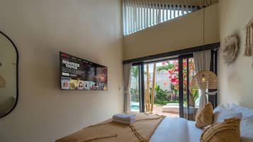 Habitación de hotel con una cama grande, un televisor empotrado mostrando una serie de Netflix y vistas a un jardín a través de una puerta corrediza de vidrio.