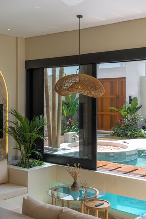 A modern living room with a glass table, a sofa, and a view of an outdoor pool area. - Villa Tigana (Pererenan)