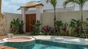 Una piscina con muelle de madera, rodeada de plantas tropicales y un muro de piedra.