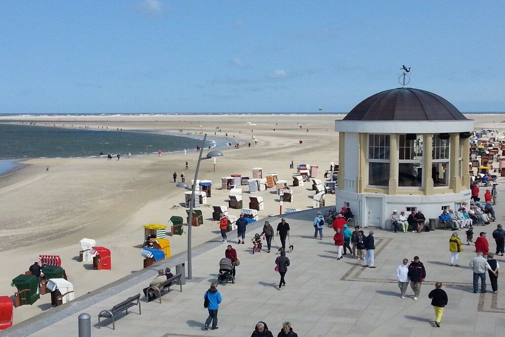 A beach promenade with a central pavilion, benches, and beach huts.