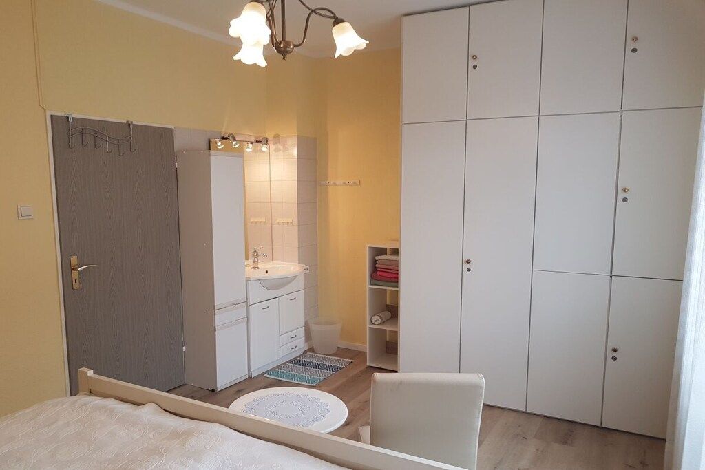 Ein Schlafzimmer mit Bett, Nachttisch, Kleiderschrank, Spiegel und einem Badezimmer mit Waschbecken und Dusche.
