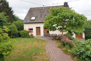 Een huis met een verhard pad dat naar de ingang leidt, omringd door groen en een kleine tuin.
