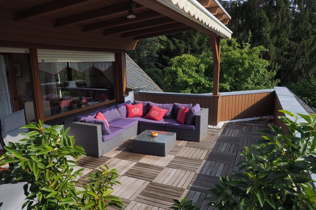 Een terras met een bank en bijzettafeltje, omgeven door houten terrassen en groen.
