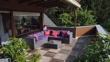 Een terras met een bank en bijzettafeltje, omgeven door houten terrassen en groen.