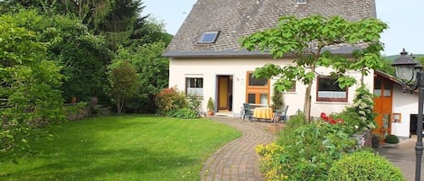 A two-story house with a paved driveway leading to a front door, surrounded by a well-maintained garden and trees.