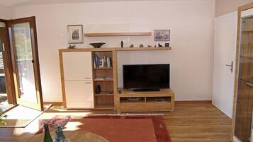 Een woonkamer met een televisie, een houten dressoir en een schuifdeur met glas.