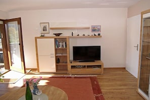 Een woonkamer met een televisie, een houten dressoir en een schuifdeur met glas.