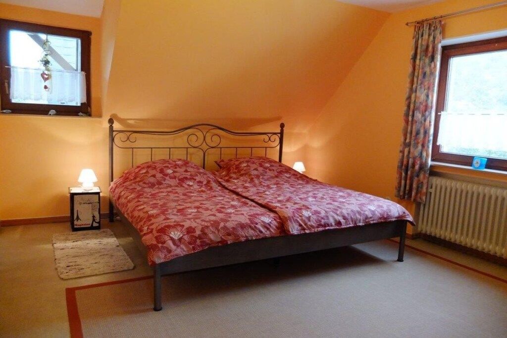 Een slaapkamer met een bed, twee bedlampen, een raam met gordijnen en een radiator.