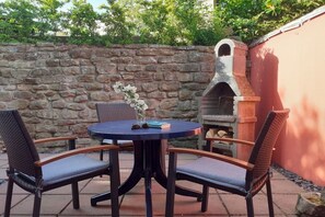 Une terrasse avec une table ronde et quatre chaises, un mur en pierre et un four en briques.
