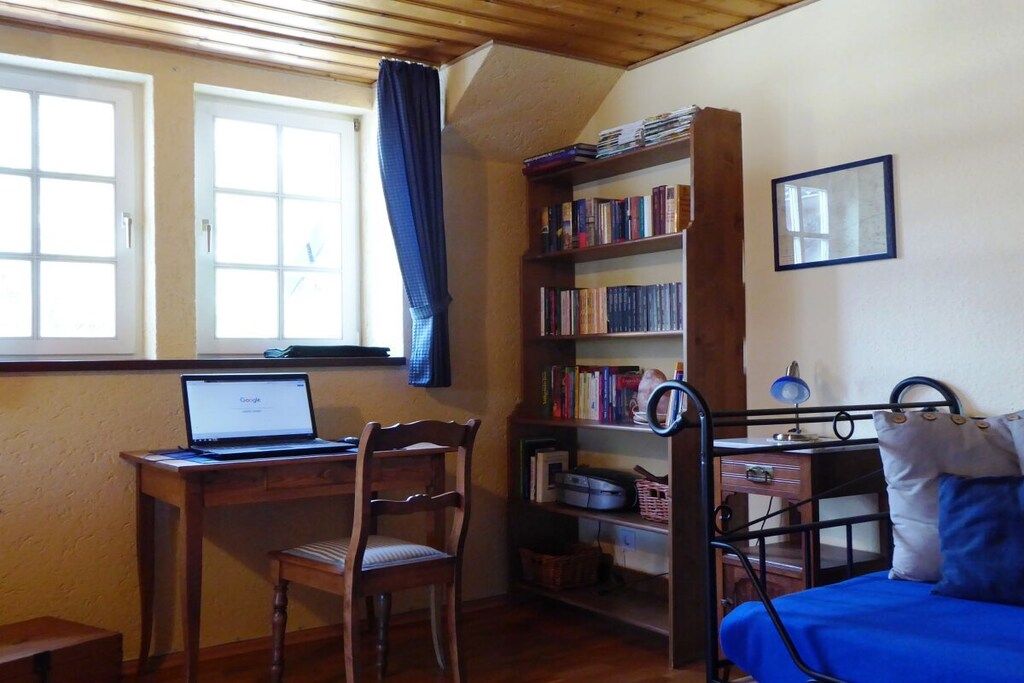 A room with a desk, chair, bookshelf, bed, and a window with curtains.
