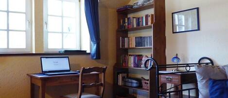 Una habitación con escritorio, silla, estantería, cama y ventana con cortinas.